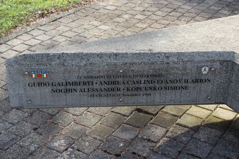 Monumento dedicato ai caduti partigiani, con nomi incisi su una base in cemento, circondato da un'area verde.