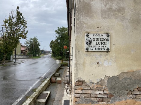 Lapide dedicata a Guizzon, con scritta commemorativa su un edificio all'angolo di una strada.