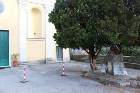 Monumento ai caduti di Morego circondato da recinzione, situato accanto a una chiesa e a un albero.