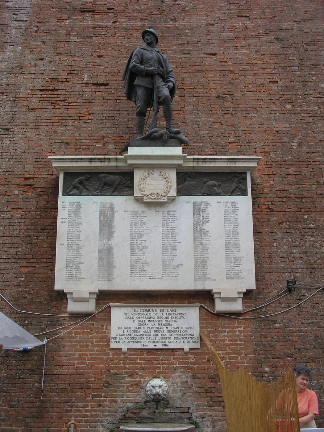 Lapide commemorativa con elenchi di caduti e statua, simbolo di onore e memoria degli eroi.