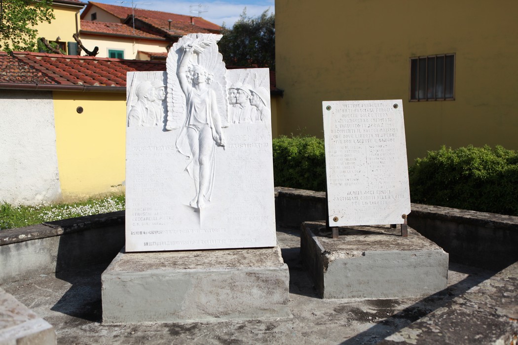 Monumento ai caduti di Soci, con statue e iscrizioni commemorative in un contesto urbano.