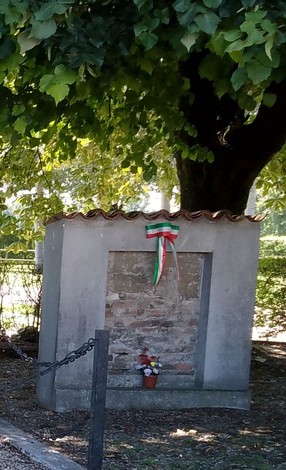 Monumento ai caduti di Villa Pompeiana e Cagnola, adornato da fiori e una fascia tricolore, immerso nel verde.