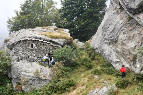 Rifugio partigiano "Non si vede" immerso nella natura, circondato da rocce e vegetazione. Persone in esplorazione.