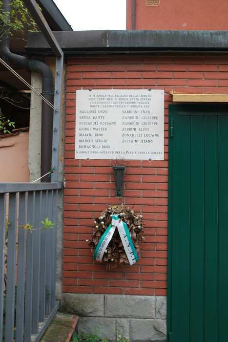 Lapide commemorativa dedicata ai partigiani della 7° GAP, con corona di fiori e ambiente circostante.