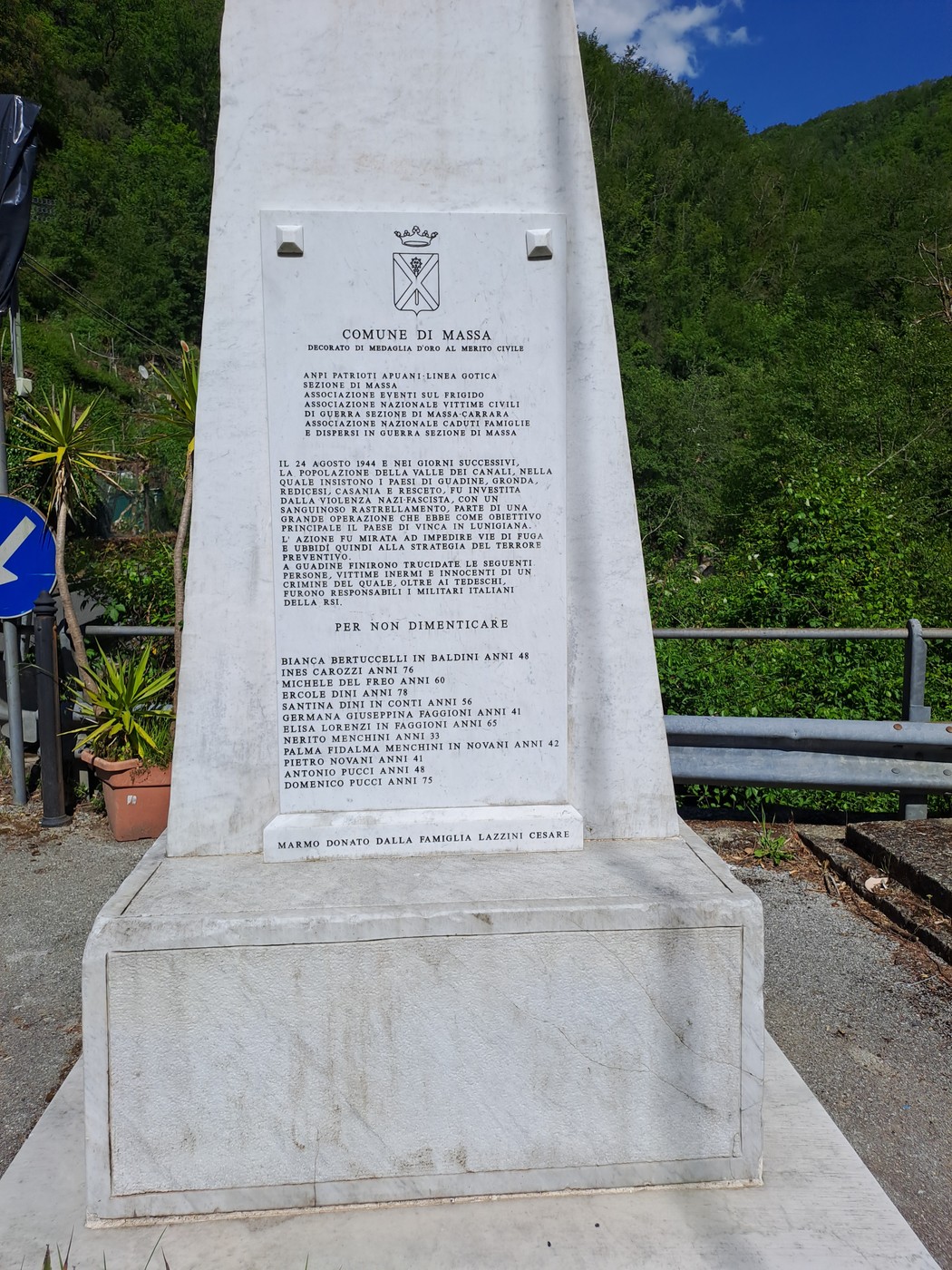 Monumento ai caduti di Guadine, una stele bianca con iscrizioni commemorative e verdeggiamento circostante.