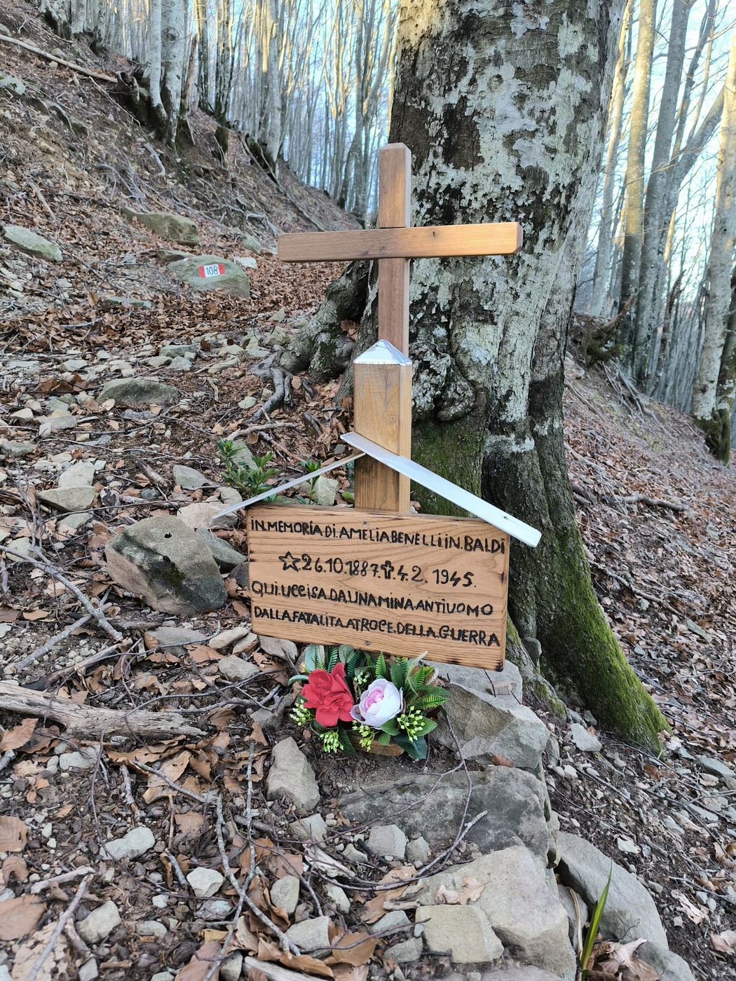 Croce commemorativa in memoria di Lino Baldi, situata nella natura, tra alberi e sentieri.