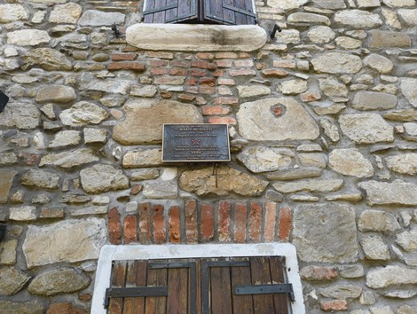 Targa su muro in pietra, dedicata a Musolesi, con finestre chiuse e dettagli in mattoni rossi.