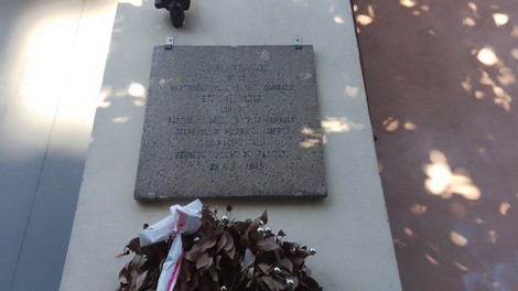 Lapide commemorativa dedicata a Guaraldi e Mozzi, apposta su una parete, con fiori accanto.