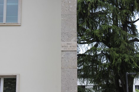 Targa con il nome di "Viale Natale Betelli" su un muro accanto a un albero verde.