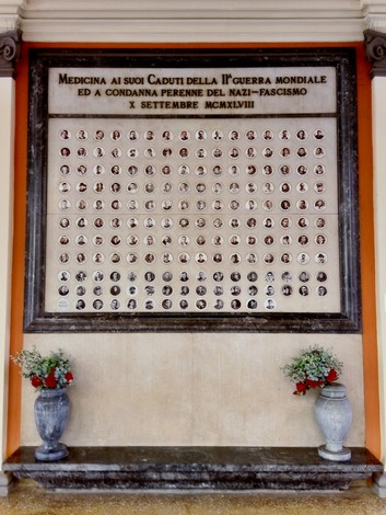 Monumento commemorativo con fotografie dei caduti nella Prima Guerra Mondiale, decorato con fiori e lapidi.