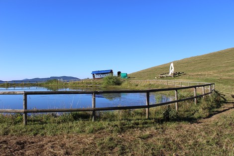 Monumento all'aviolancio di Cadorna su un prato verde con un lago, una struttura e sfondo montagne.