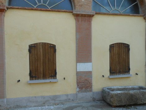Lapide commemorativa di Azzolini su una parete di edificio con finestre chiuse da persiane in legno.