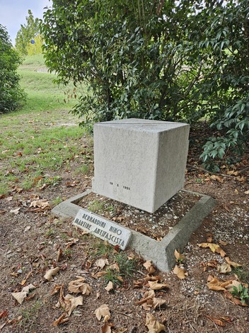 Monumento in pietra dedicato a Bernardini, circondato da vegetazione e foglie secche.