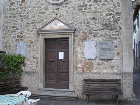 Lapide a Gagliardi su una parete in pietra, accanto a una porta in legno, ambientazione storica.