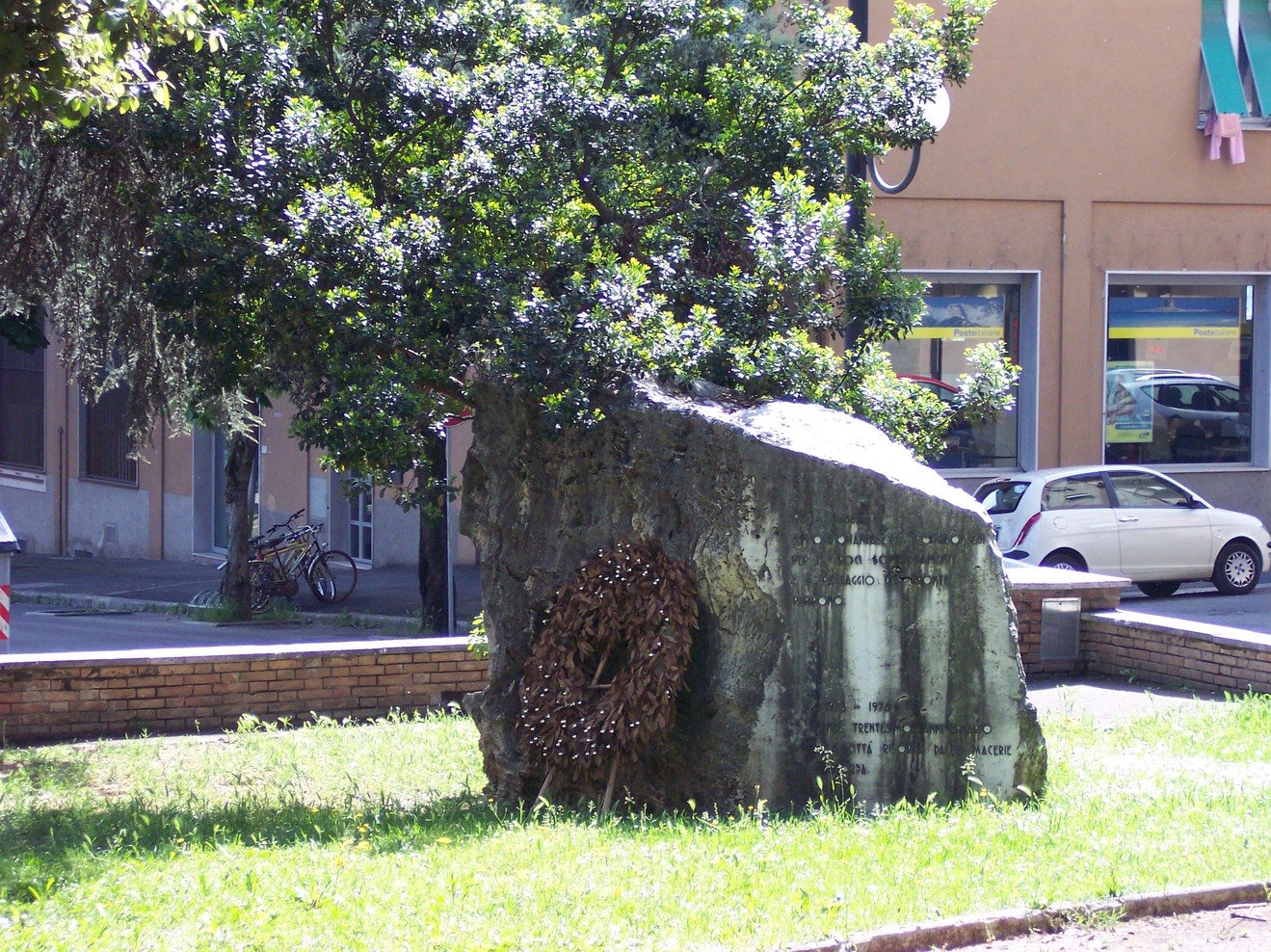 Monumento ai caduti per i bombardamenti, situato in un'area verde tra alberi e strade urbane.