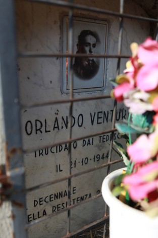 Cippo commemorativo dedicato a Orlando Venturi, con una fotografia e fiori decorativi.