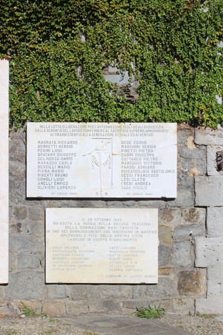 Lapide commemorativa dedicata all'Ansaldo Meccanico, con nomi e date di caduti. sfondo di vegetazione.