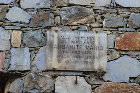 Lapide in pietra dedicata alla memoria del partigiano Bassanite Mario, situata su un muro di pietra.