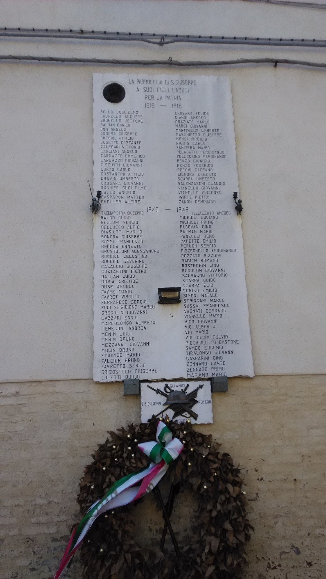 Lapide commemorativa dedicata ai caduti di San Giuseppe, con elenco di nomi e decorazioni floreali.