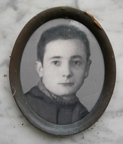 Ritratto di un giovane, incorniciato in un ovale, su un cippo commemorativo. Atmosfera nostalgica e storica.