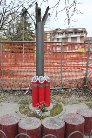 Monumento ai tre martiri con struttura centrale e tre colonne rosse, circondato da un recinto e fiori.