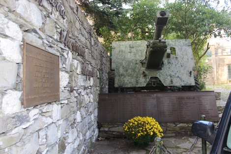 Monumento ai caduti di Bavari, con una cannone e lapidi commemorative tra la vegetazione.