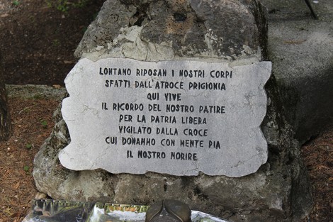 Un monumento in pietra dedicato ai caduti per la libertà, immerso nel verde, con iscrizioni commemorative.