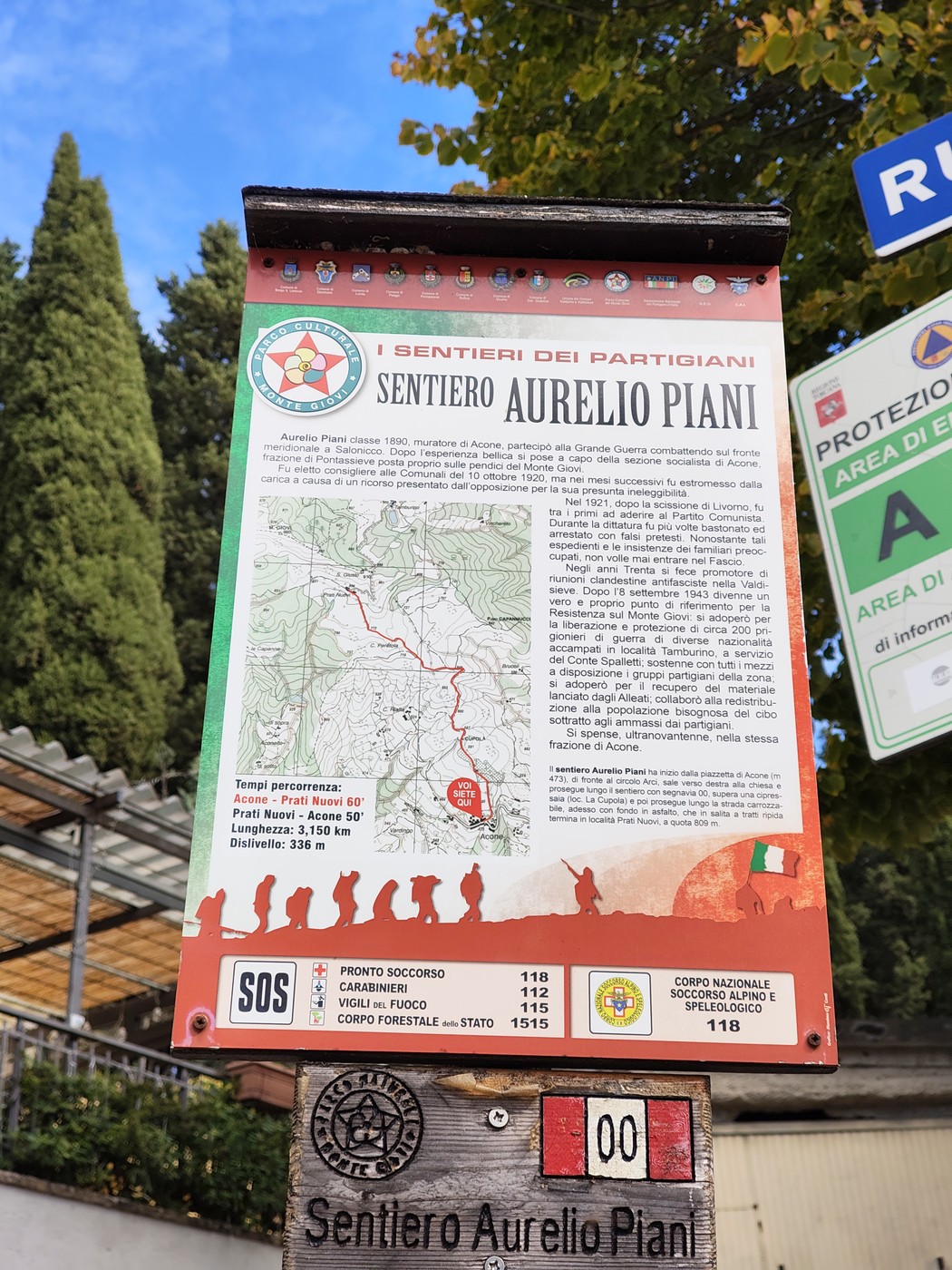 Cartello informativo con mappa e testo dedicato al Sentiero Aurelio Piani, su palo in un'area alberata.