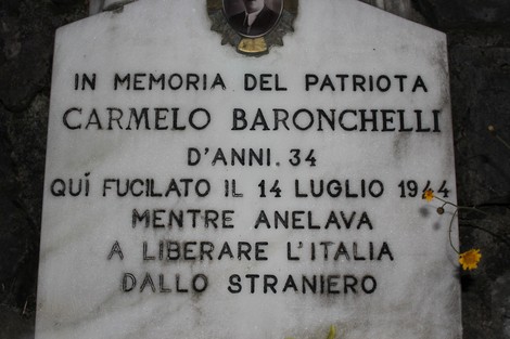 Lapide commemorativa dedicata a Carmelo Baronchelli, patriota fucilato nel 1944, immersa nella natura.
