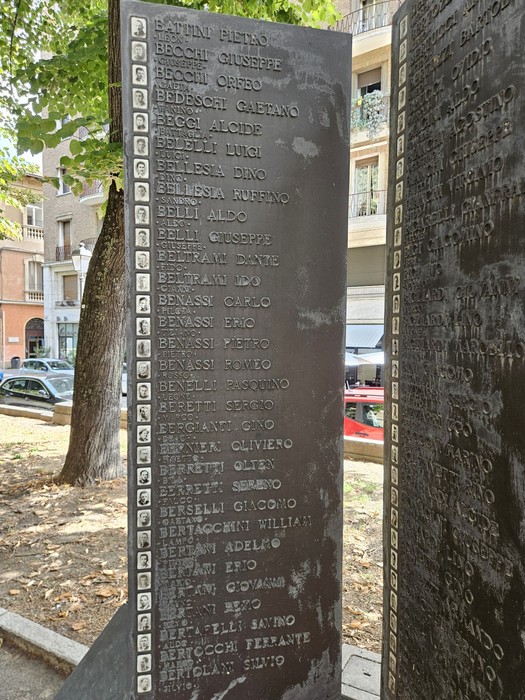 Pannello in pietra inciso con i nomi dei caduti, parte del Sacrario della Resistenza Reggiana in uno spazio alberato.