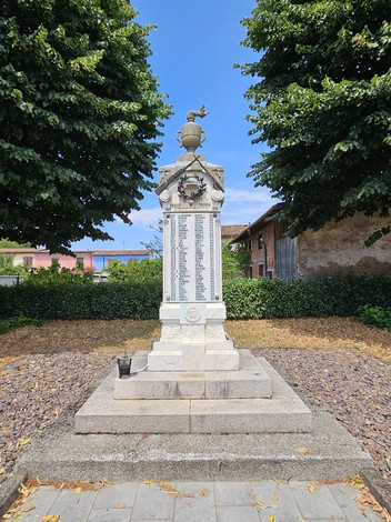 Monumento ai Caduti di Corno Giovine, con pregiata scultura e nomi incisi, contornato da alberi e un cielo sereno.