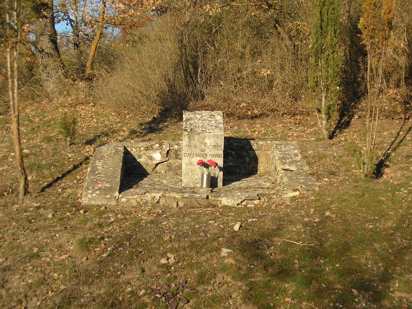 Cippo commemorativo situato in una zona boschiva, circondato da una base di pietre.