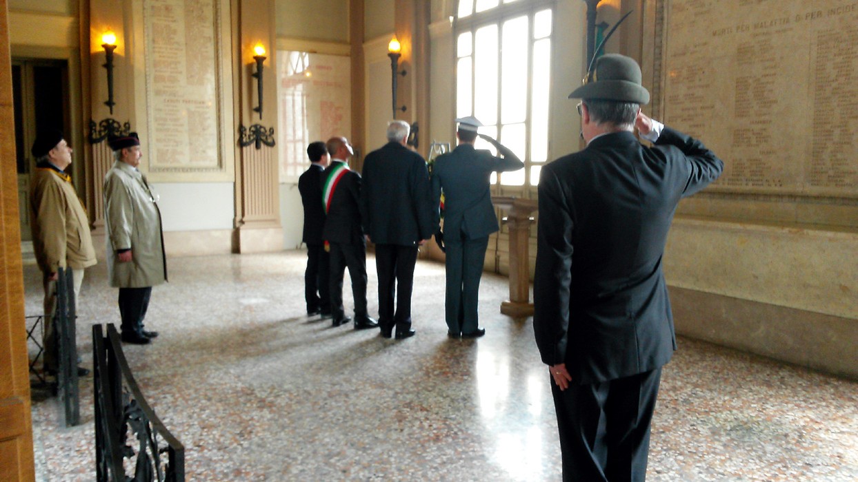 Cerimonia di commemorazione presso la lapide ai caduti di Voghera, con autorità e cittadini in attesa di omaggio.