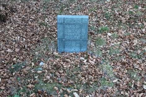 Cippo commemorativo in pietra circondato da foglie secche nel contesto naturale di Valdo.