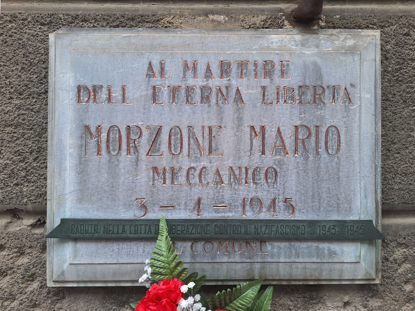 Lapide commemorativa dedicata a Mario Morzone, martire della libertà, decorata con fiori e un nastro.