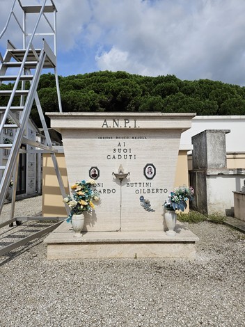 Sacrario dei Partigiani con lapide commemorativa e decorazioni floreali, immerso in un ambiente tranquillo.