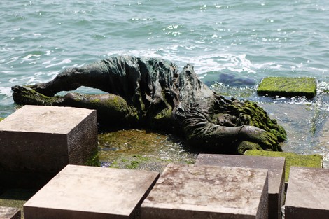 Monumento alla partigiana, scultura in bronzo che rappresenta una figura distesa vicino all'acqua, circondata da blocchi di pietra.