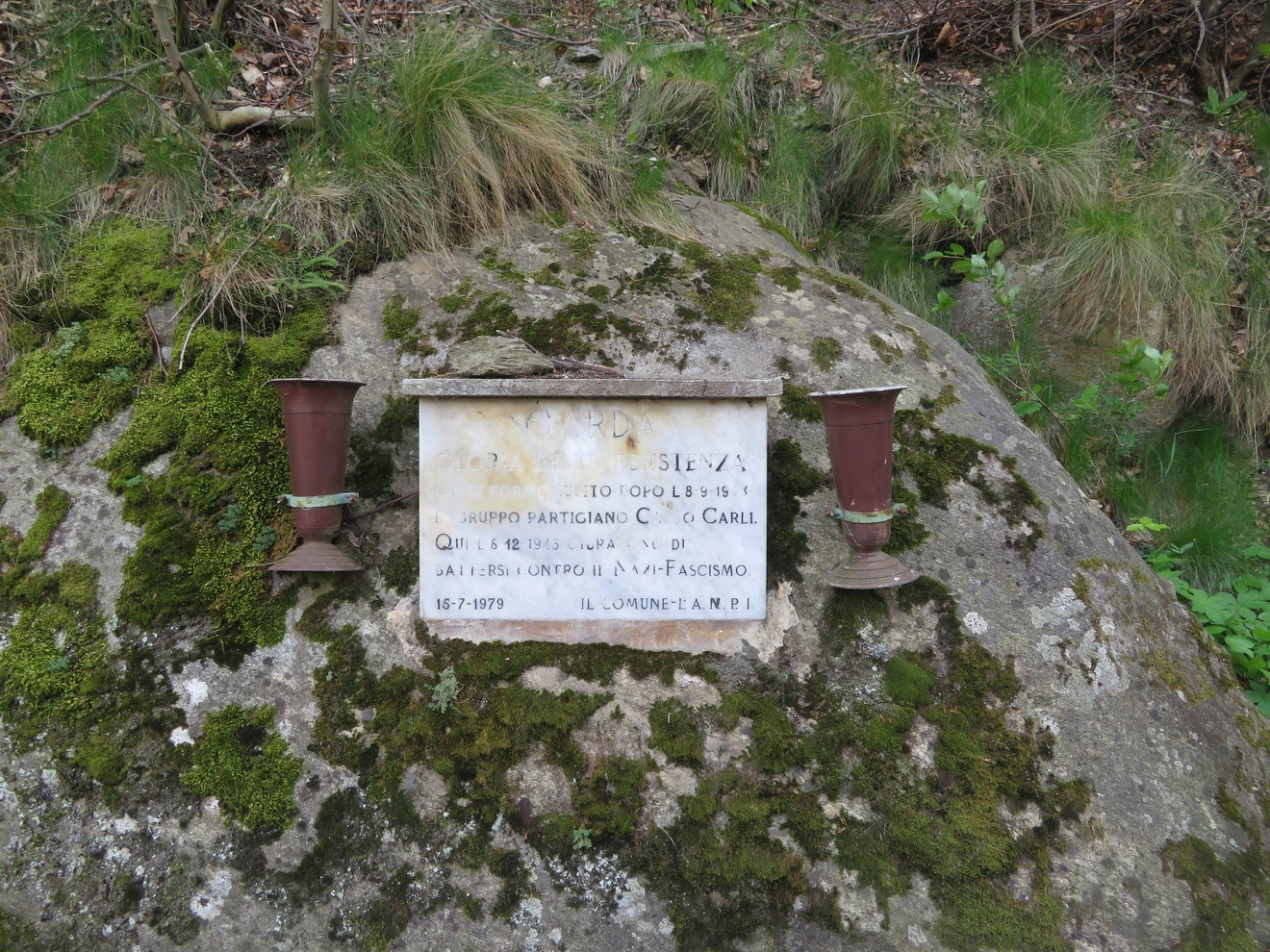 Lapide commemorativa che ricorda il giuramento dei partigiani contro il fascismo. Paesaggio naturale circostante.