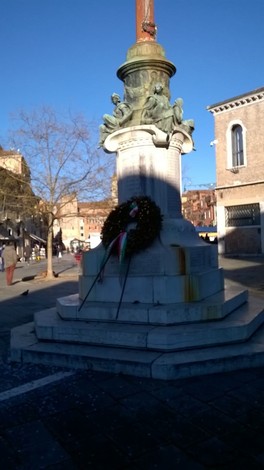 Monumento ai caduti dei Carmini, con decorazioni e un drappo tricolore, in una piazza soleggiata.