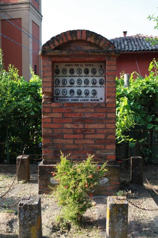 Cippo commemorativo ai caduti della Battaglia di Rasiglio, in un contesto rurale con vegetazione circostante.
