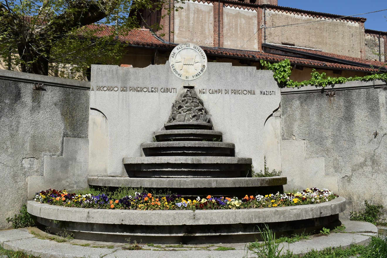 Monumento commemorativo dedicato ai caduti nei campi di prigionia, con una struttura a gradini e fiori colorati.