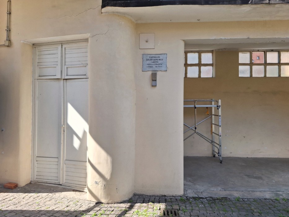 Lapide commemorativa affissa su un muro vicino a un ingresso, con area di lavoro accessoria.