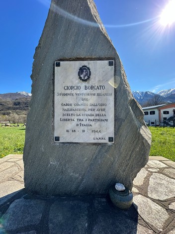 Monumento dedicato a Ciorgio Borgato, studente milanese, situato in un'area verde con montagne sullo sfondo.