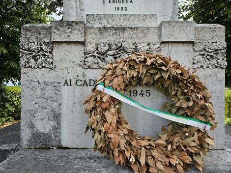 Monumento ai Caduti con corona di alloro secca e decorazioni floreali, simbolo di commemorazione.