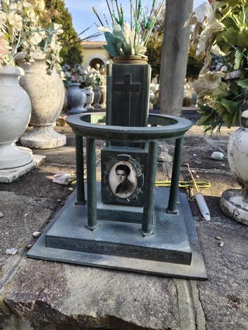 Sacrario ai caduti con monumento in bronzo e fotografie commemorative, circondato da fiori.