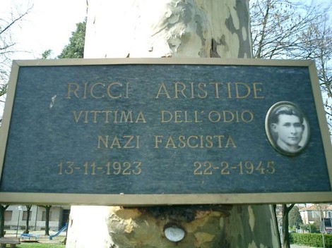 Targa commemorativa dedicata ai martiri, con nome, date di nascita e morte, affissa su un albero.