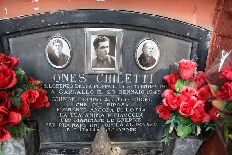 Sepolcro di Chiletti con fotografie e fiori, dedicato a Ones Chiletti, simbolo di memoria e onore.