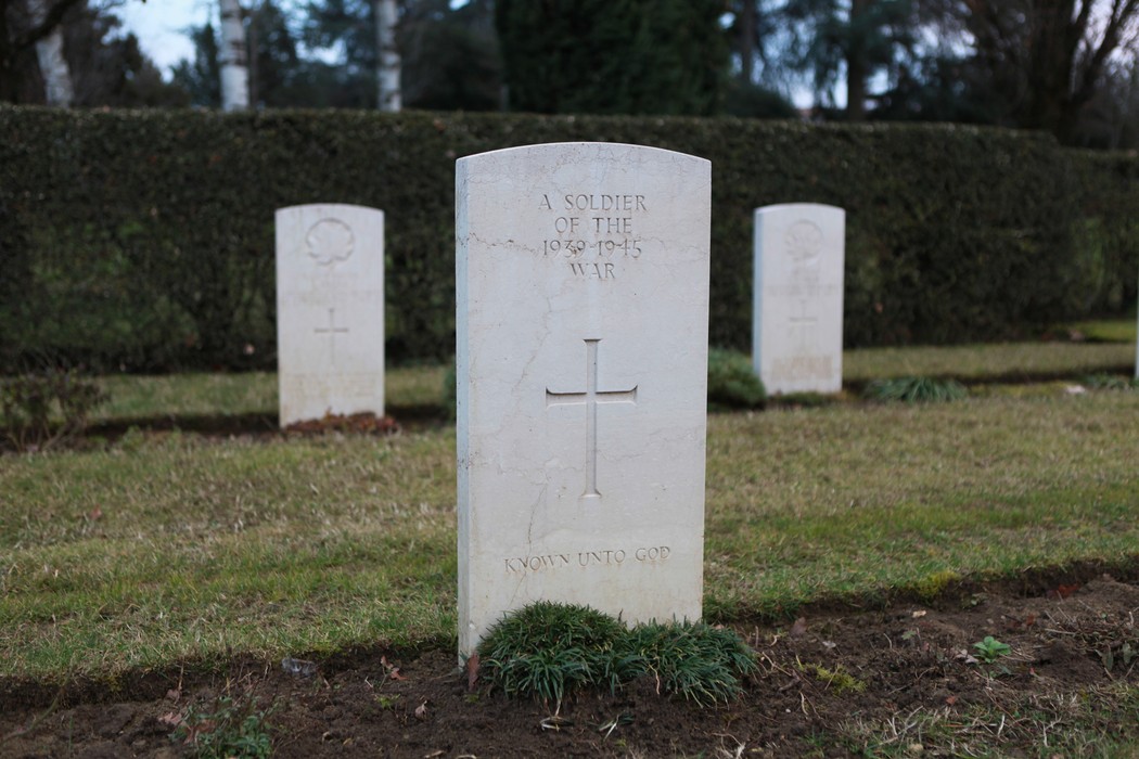 Cimitero di guerra del Commonwealth con tombe bianche e croci su un prato verde. Atmosfera di riflessione e rispetto.