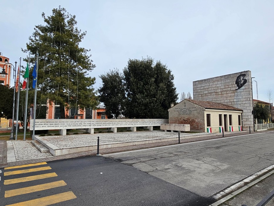 Monumento per l'eccidio di Villamarzana, con struttura architettonica e bandiere. Ambito commemorativo e storico.