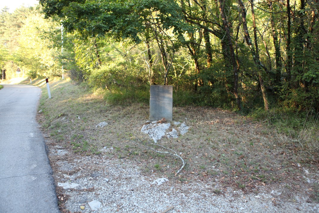 Cippo commemorativo dedicato a Pandolfo e Lonari, immerso nella natura lungo una strada.